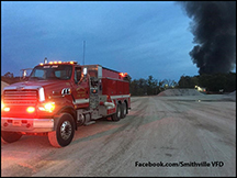 Smithville VFD Tanker 55 queues to load water; smoke from the massive IEI fire looms in the background.